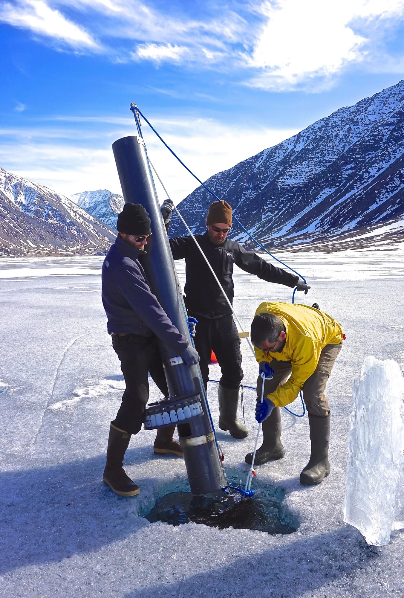 Researchers coring a frozen lake ringed by snowy mountains